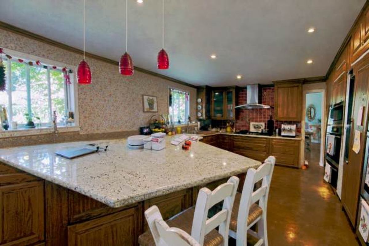 The kitchen before: dark wood cabinets, a granite island and red pendant lights