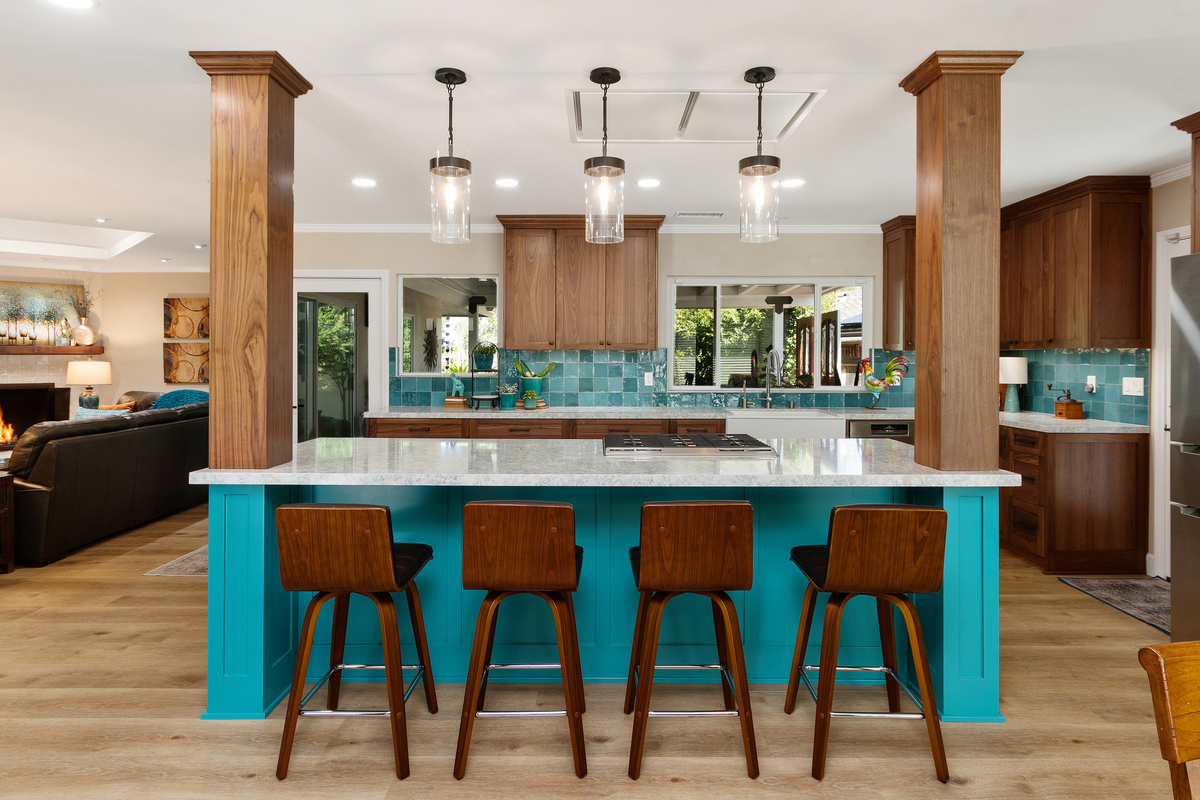 Kitchen with a teal island, walnut columns and four wood bar stools