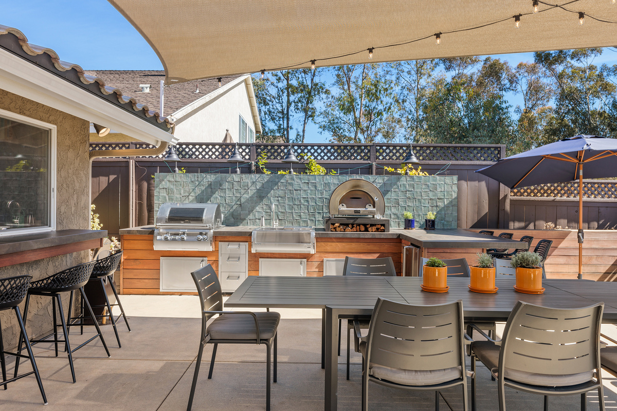 Finished: eight-seat dining table under a sail shade beside a built-in outdoor kitchen