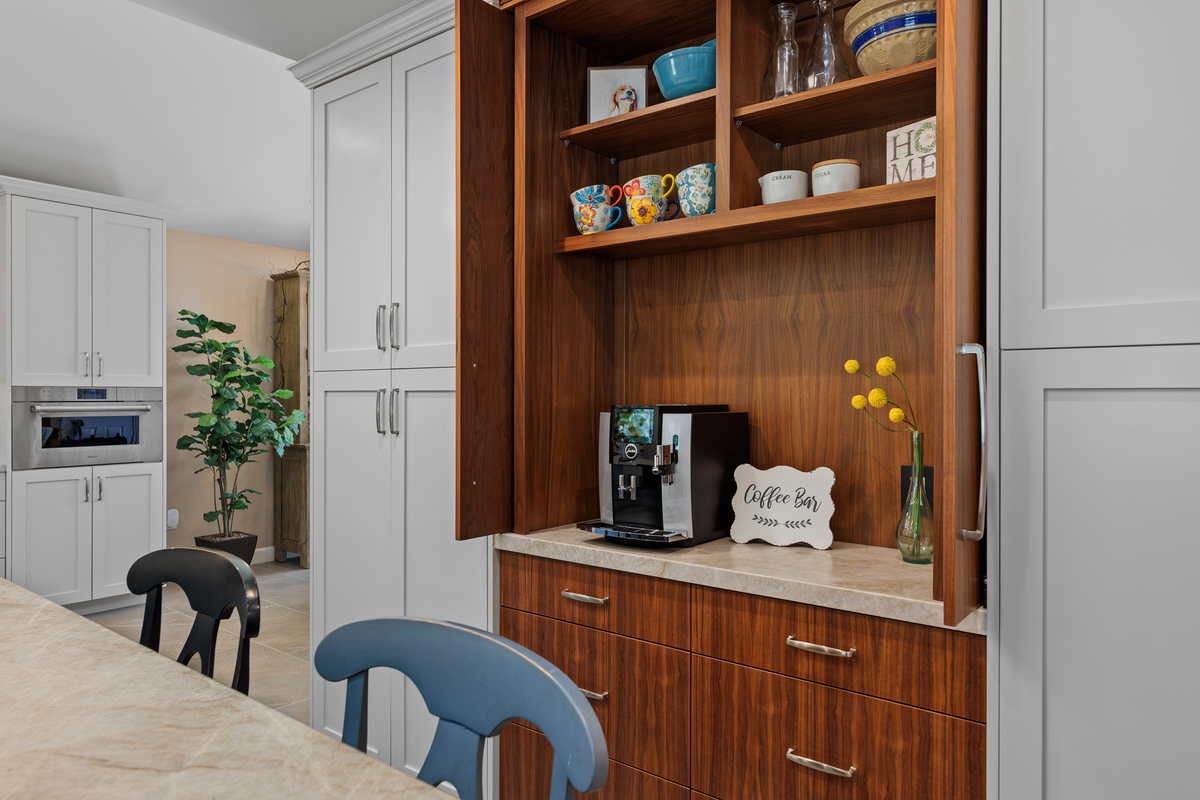 Walnut coffee bar built into white cabinetry, with an espresso machine and colorful mugs