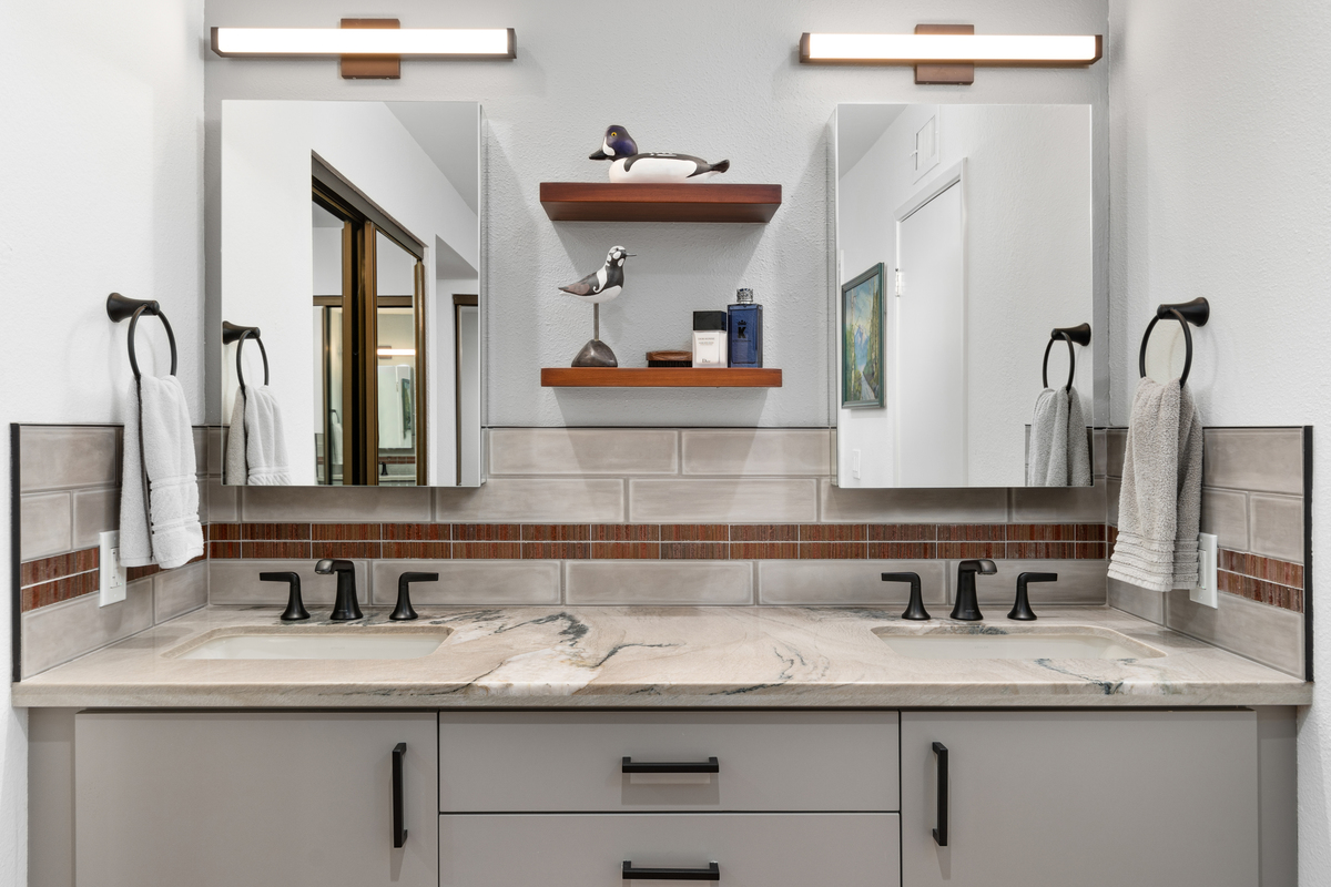 Double vanity with two framed mirrors, brass sconces and a floating wood shelf