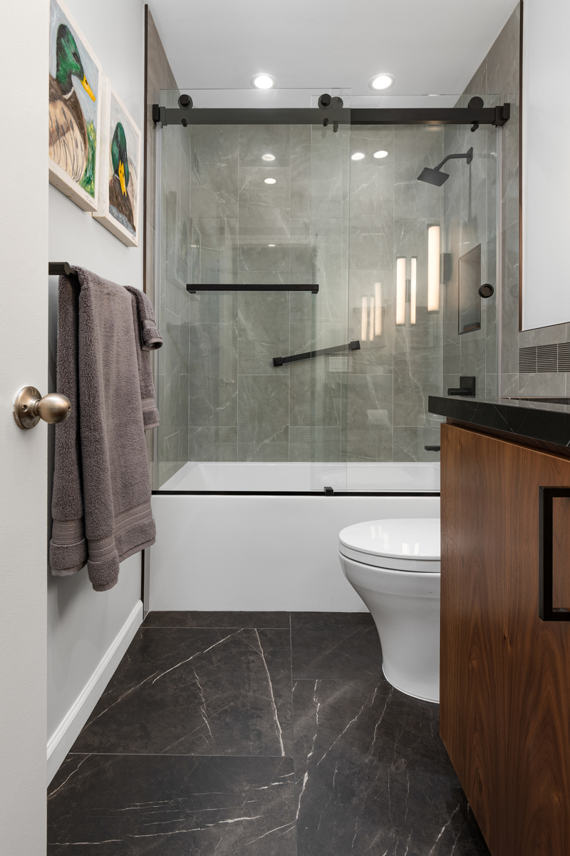Finished: walnut vanity with black counter beside a glass-door tiled shower