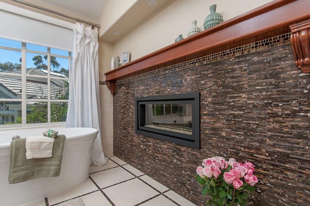 Freestanding tub beside a see-through fireplace set in dark glass tile