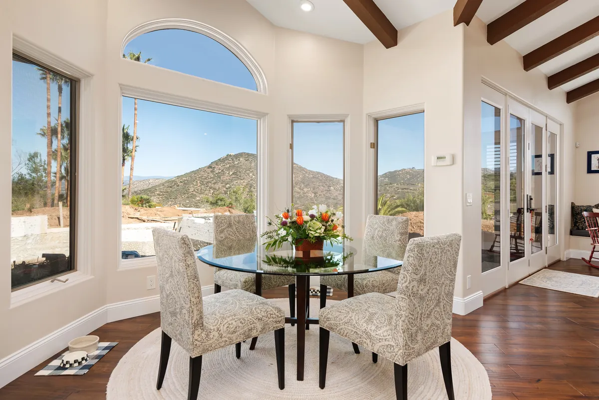 Breakfast nook with a round glass table and tall windows looking out at the hills