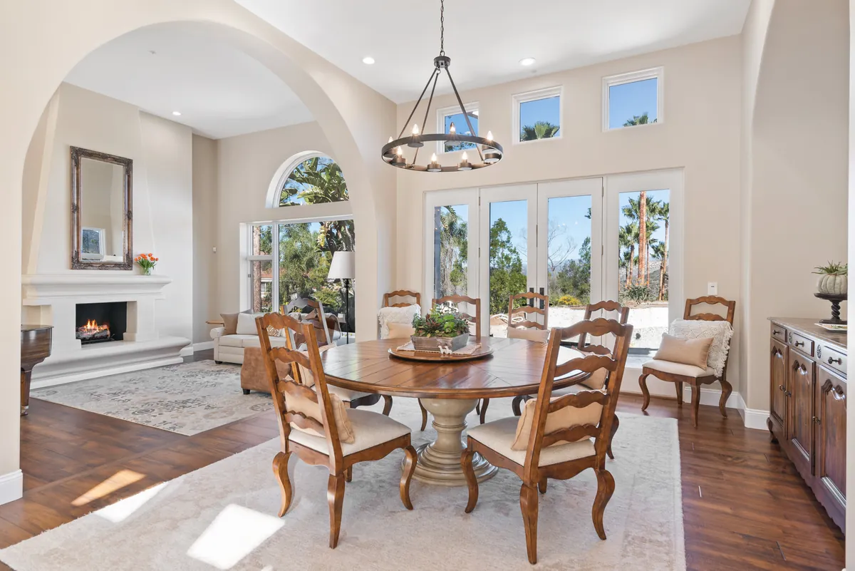 Dining room under an arch with a wrought iron chandelier and a fireplace beyond